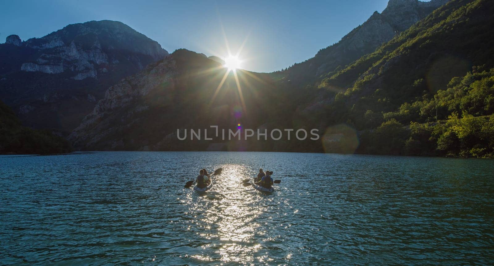 A group of friends enjoying fun and kayaking exploring the calm river, surrounding forest and large natural river canyons during an idyllic sunset. by dotshock