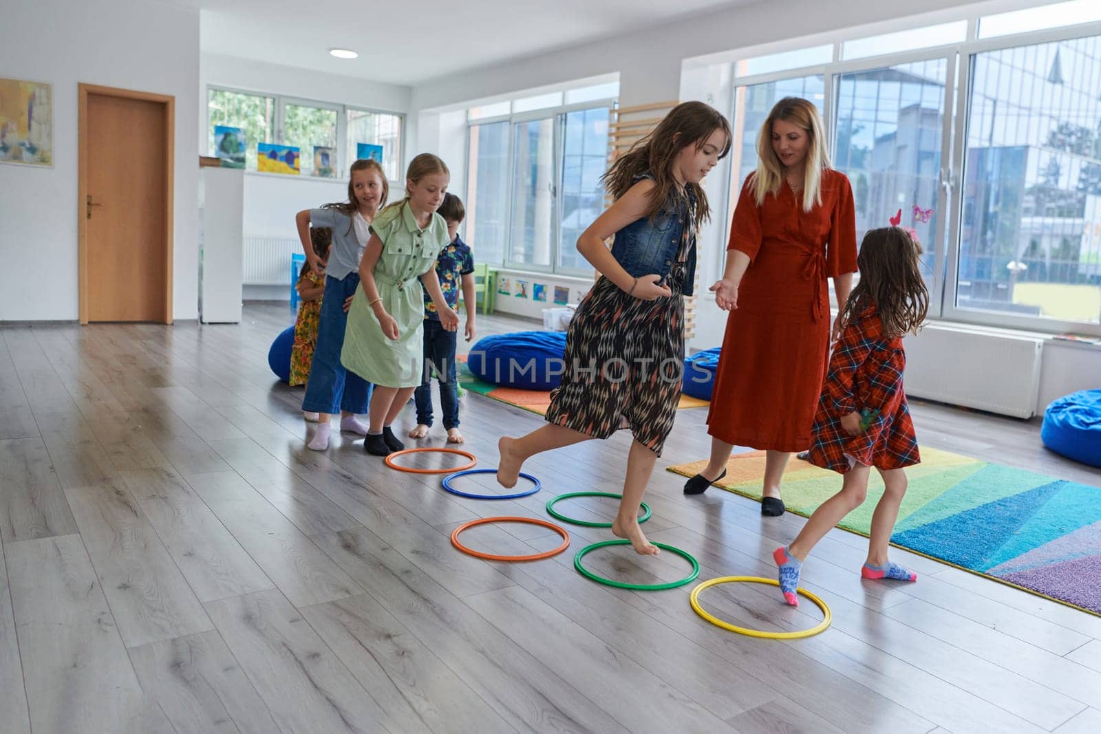 Small nursery school children with female teacher on floor indoors in classroom, doing exercise. Jumping over hula hoop circles track on the floor