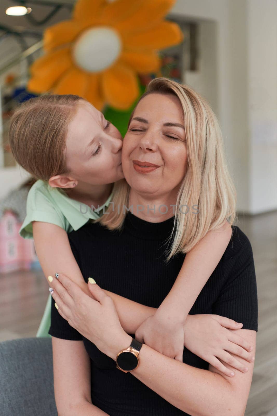 A cute little girl kisses and hugs her mother in preschool. High quality photo