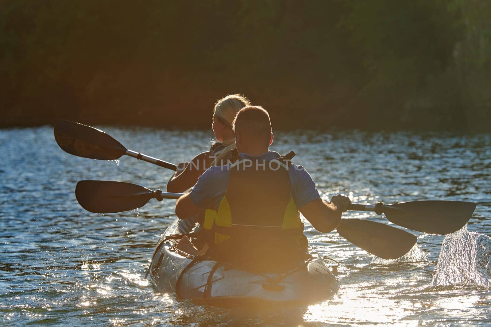 A young couple enjoying an idyllic kayak ride in the middle of a beautiful river surrounded by forest greenery in sunset time by dotshock