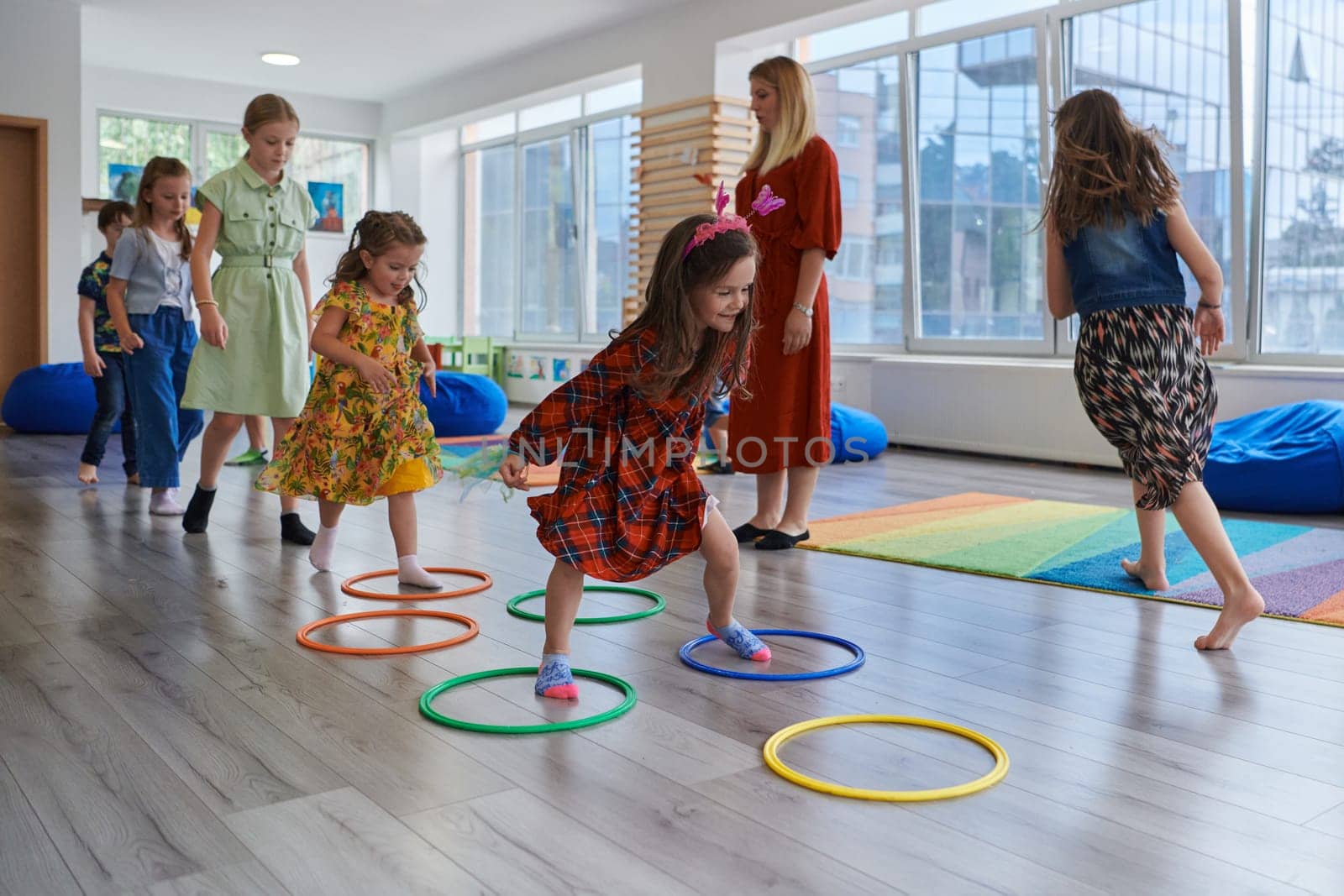 Small nursery school children with female teacher on floor indoors in classroom, doing exercise. Jumping over hula hoop circles track on the floor