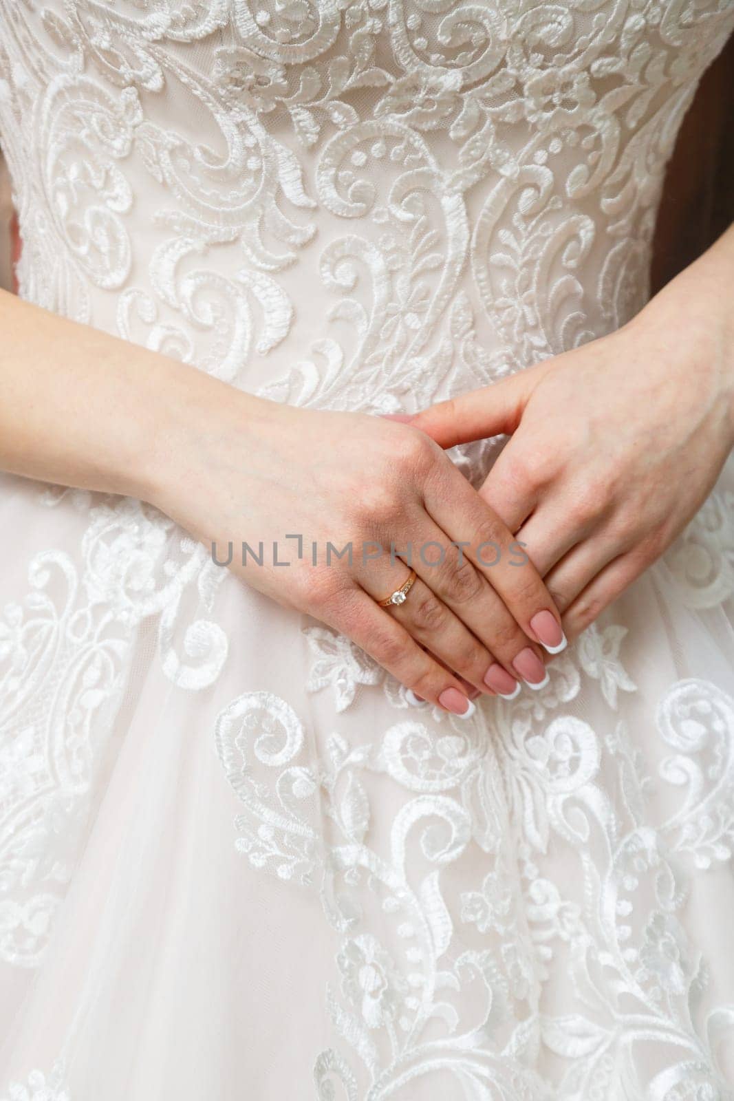 Bride's hands folded on a white wedding dress by Dmitrytph