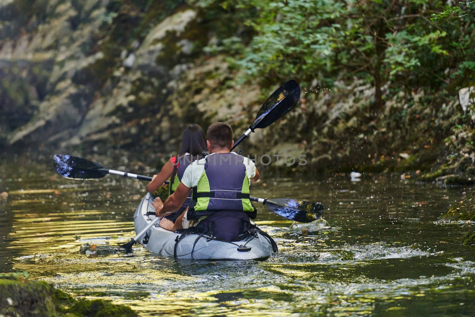 A young couple enjoying an idyllic kayak ride in the middle of a beautiful river surrounded by forest greenery by dotshock