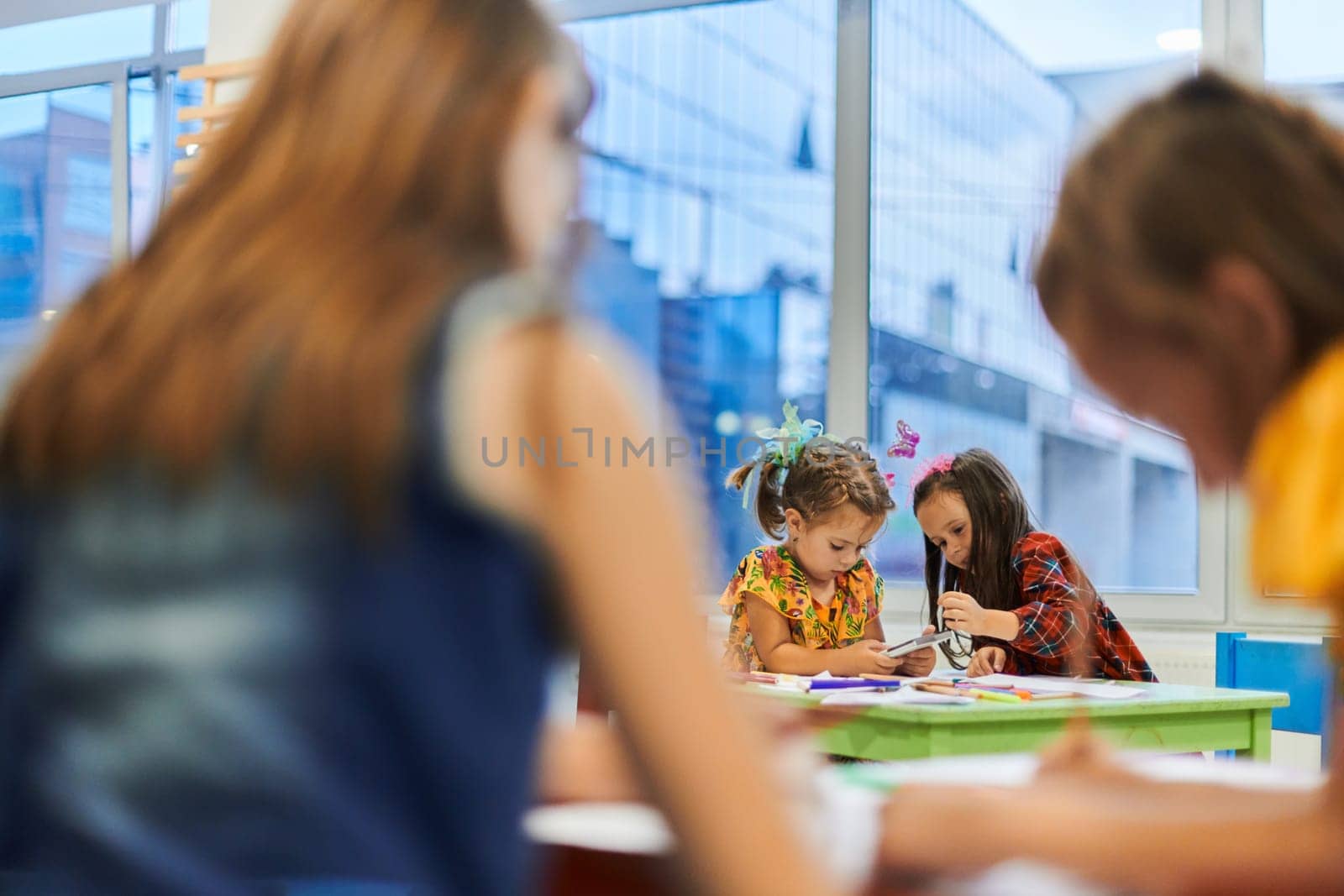 Creative kids during an art class in a daycare center or elementary school classroom drawing with female teacher