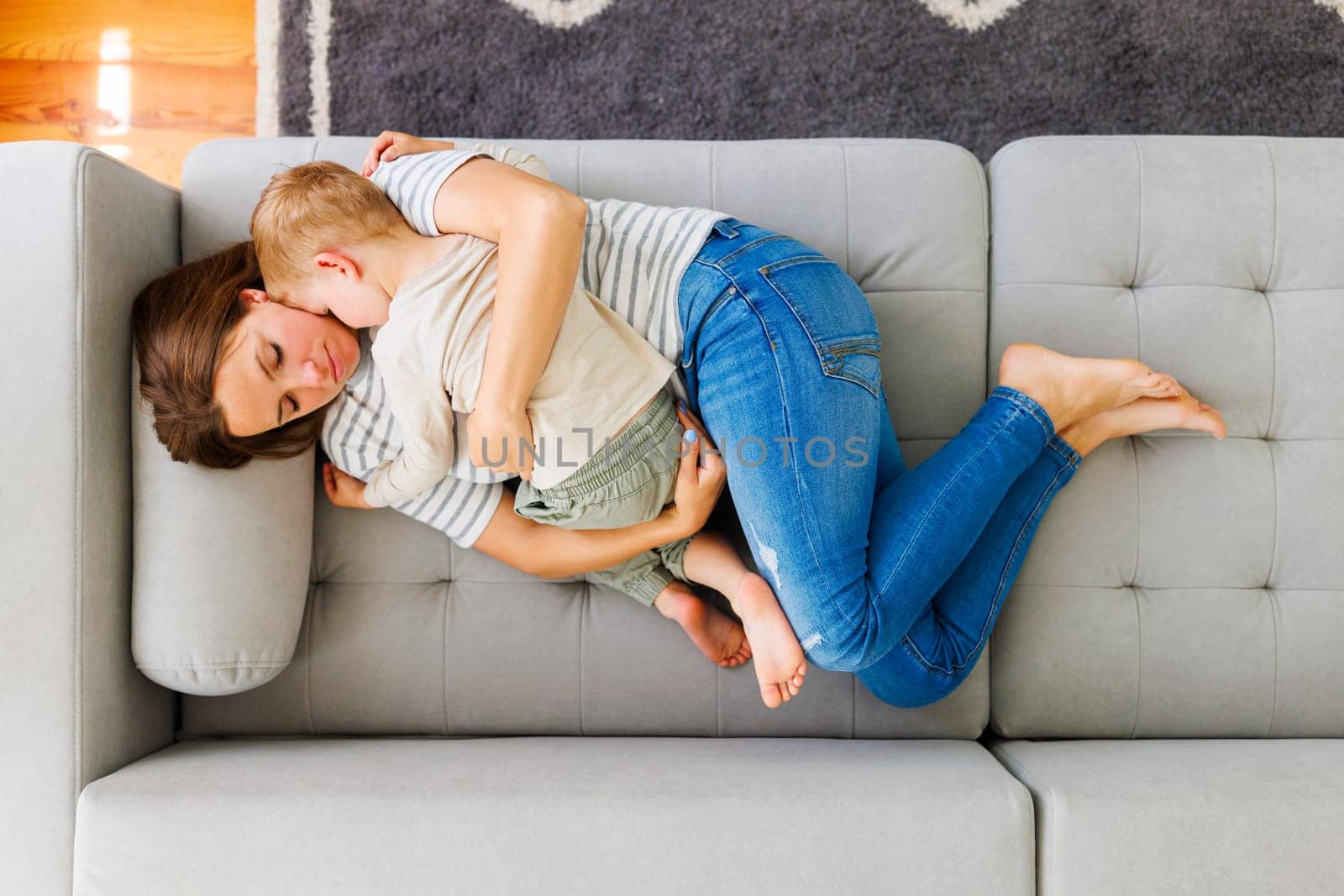 Mother embraces her cute little son while laying together on the couch in the living room