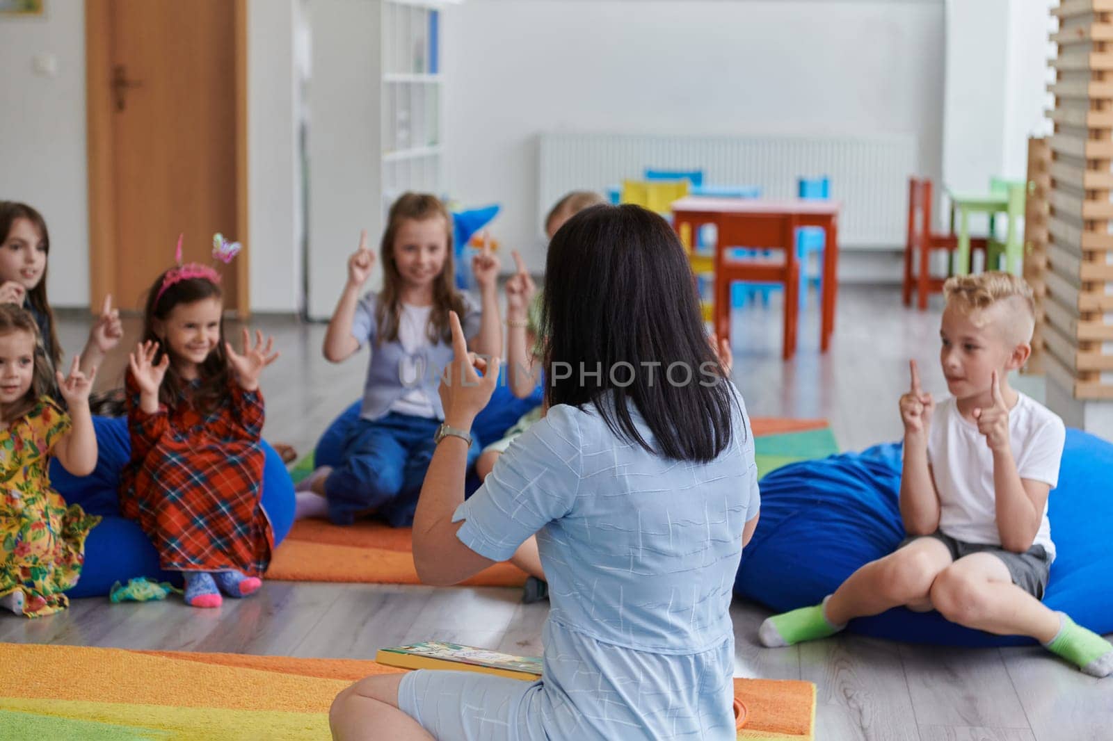 A happy female teacher sitting and playing hand games with a group of little schoolchildren by dotshock