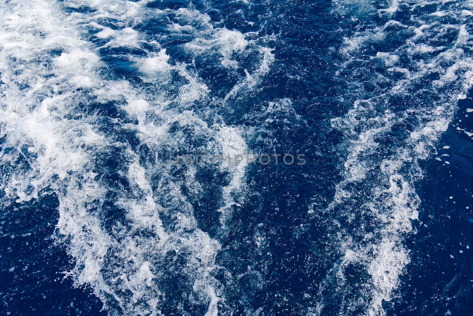 Abstract blue sea water with white waves. Blue sea texture with waves and foam. Rough deep turquoise and blue Mediterranean sea. Sea water top view.