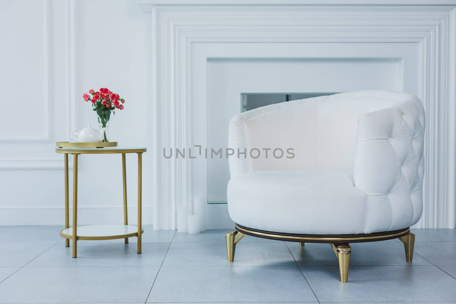 Photo of a beautifully decorated table with a bouquet of red flowers and a teapot with cups. White easy chair by Dmitrytph