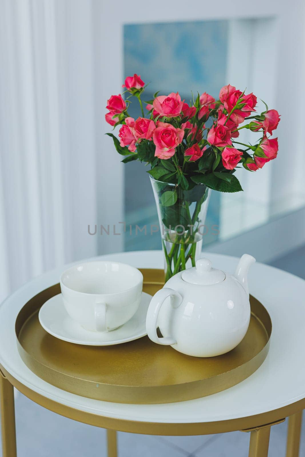 A table with a white teapot and a white cup. on the table a vase with fresh flowers by Dmitrytph