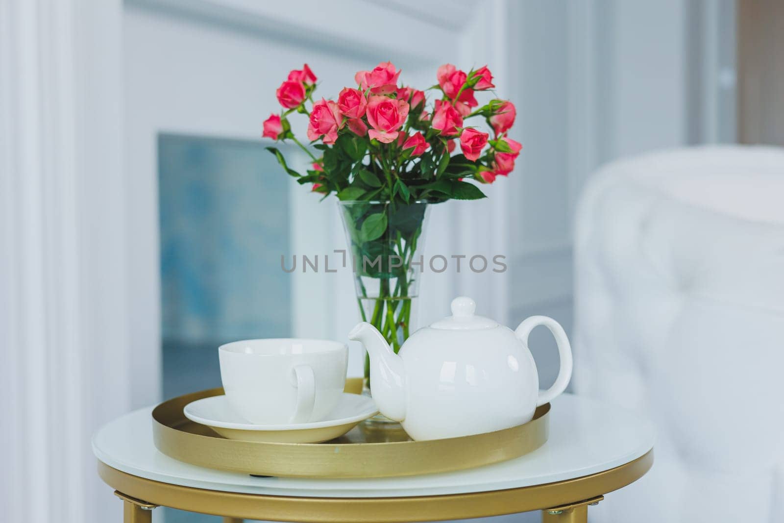 A table with a white teapot and a white cup. on the table a vase with fresh flowers by Dmitrytph