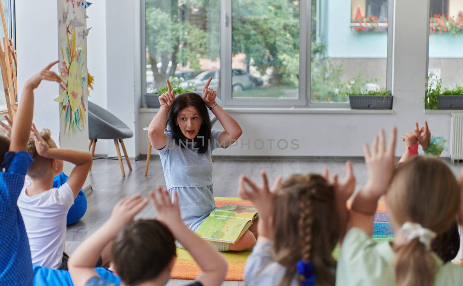 A happy female teacher sitting and playing hand games with a group of little schoolchildren.