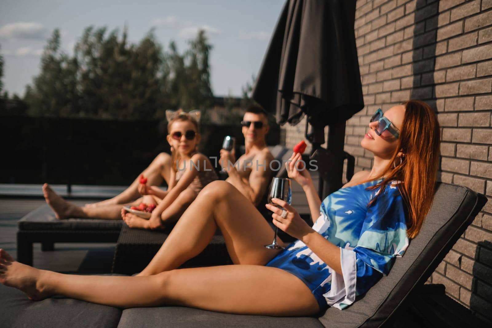 A happy family in swimsuits sunbathe in summer on their terrace on sun beds.