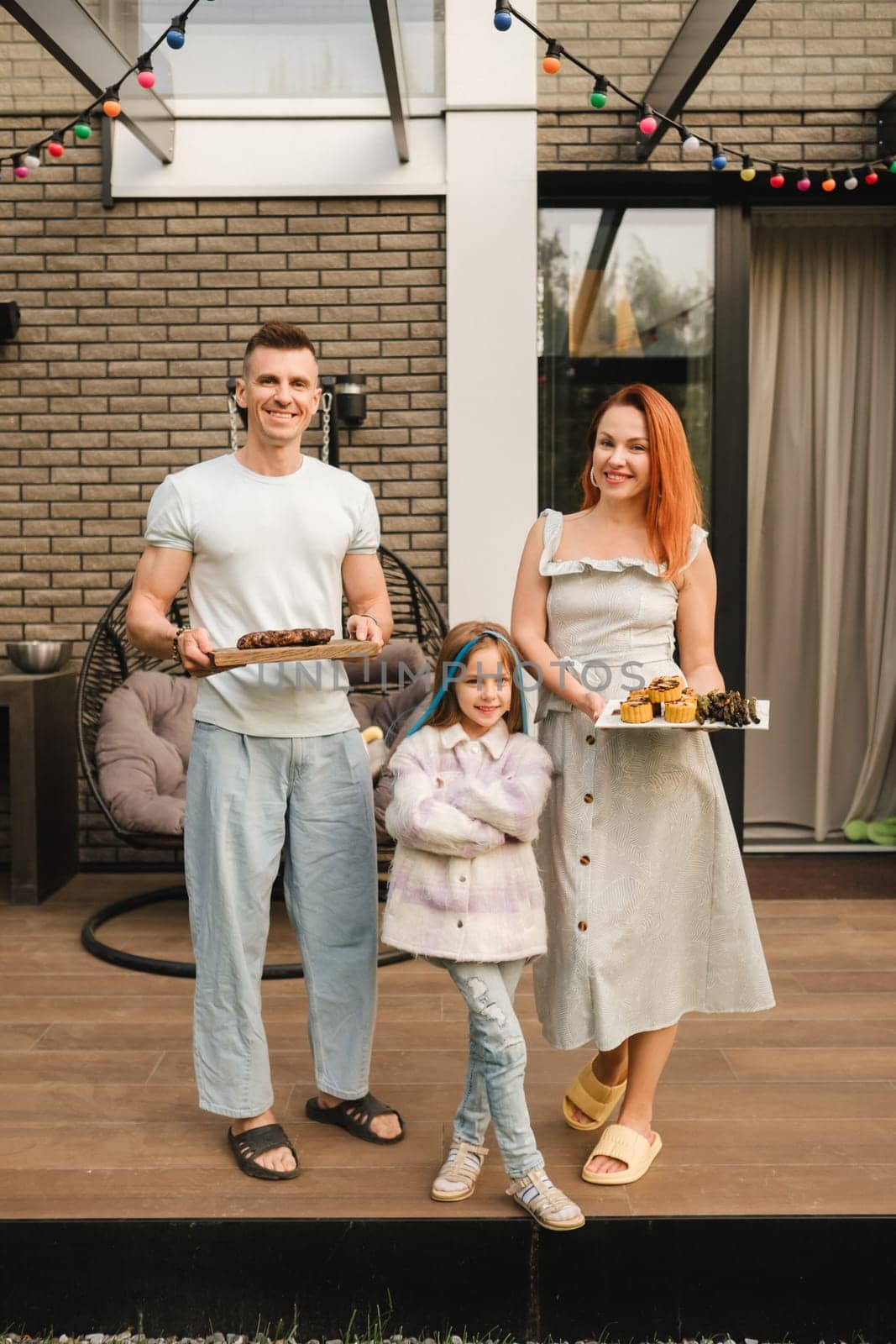 A happy family has prepared lunch and will eat at their house. Portrait of a family with food in their hands by Lobachad