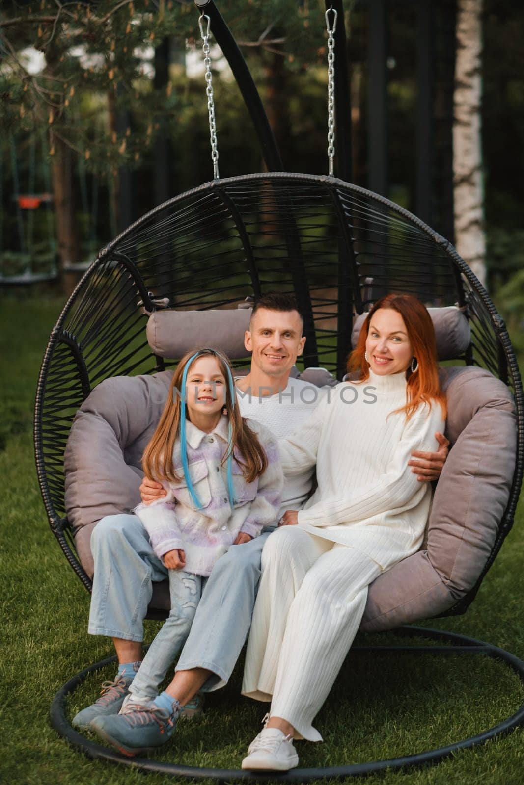 A happy family is sitting in a hammock on the lawn near the house by Lobachad