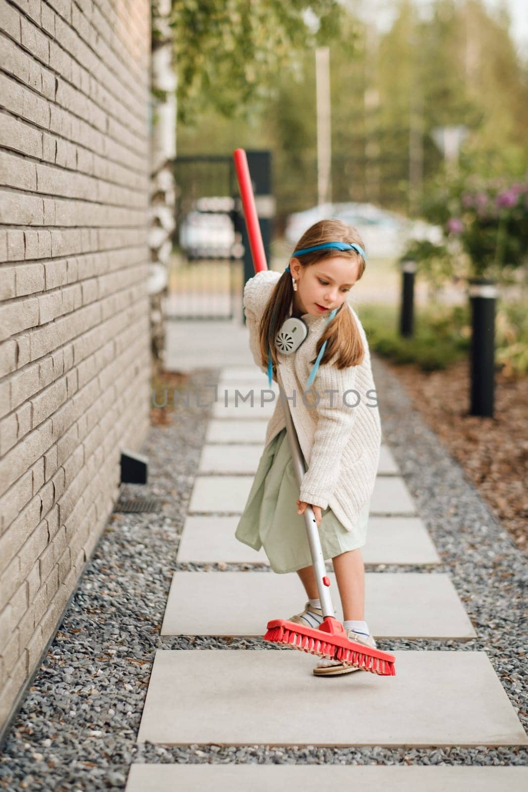 A little girl with a brush cleans a path on the street in the courtyard.