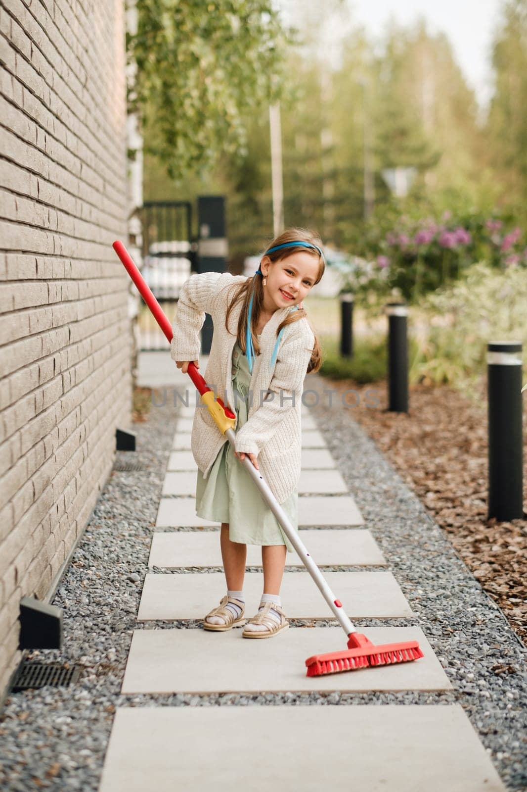 A little girl with a brush cleans a path on the street in the courtyard.