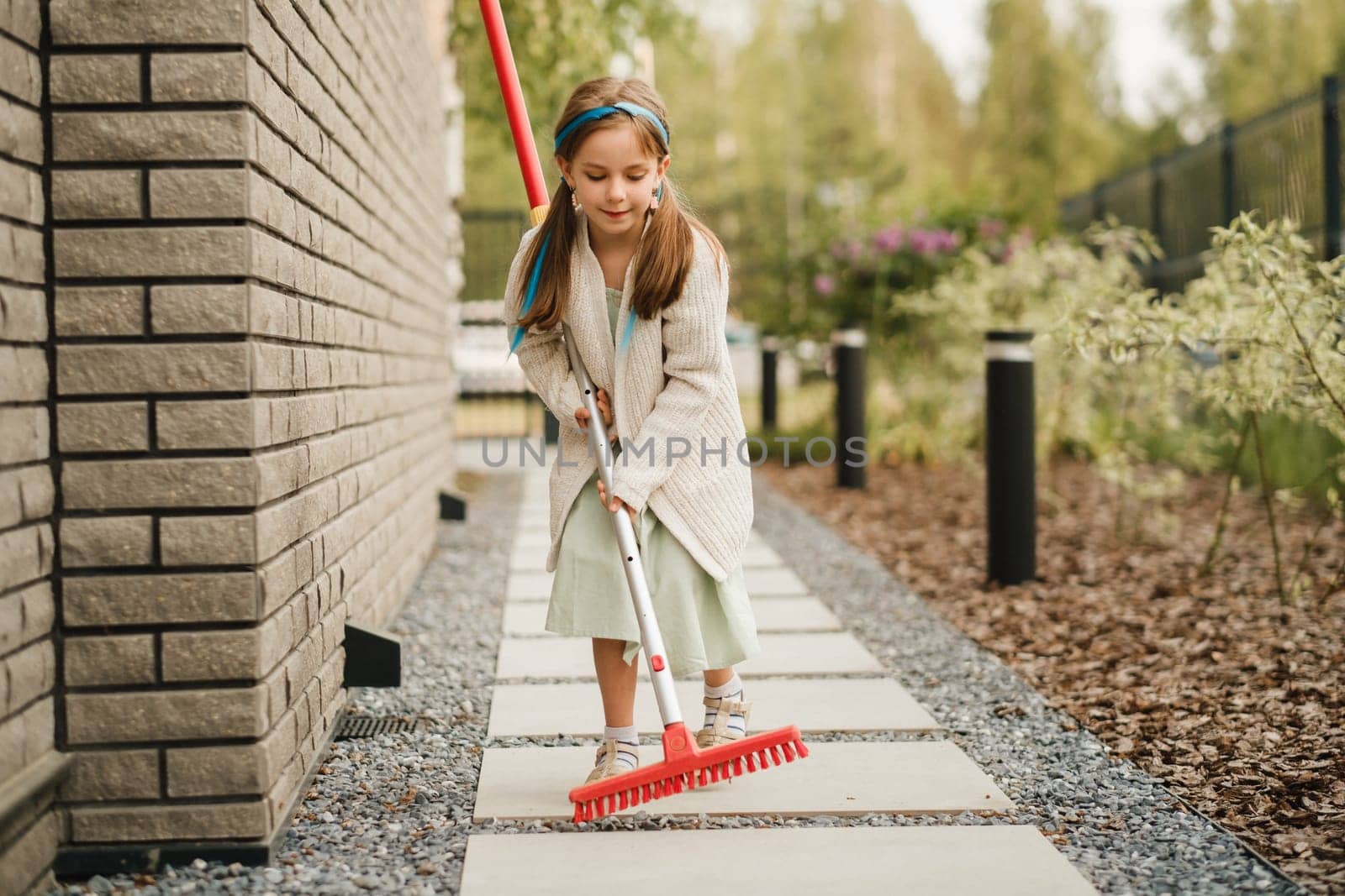 A little girl with a brush cleans a path on the street in the courtyard.