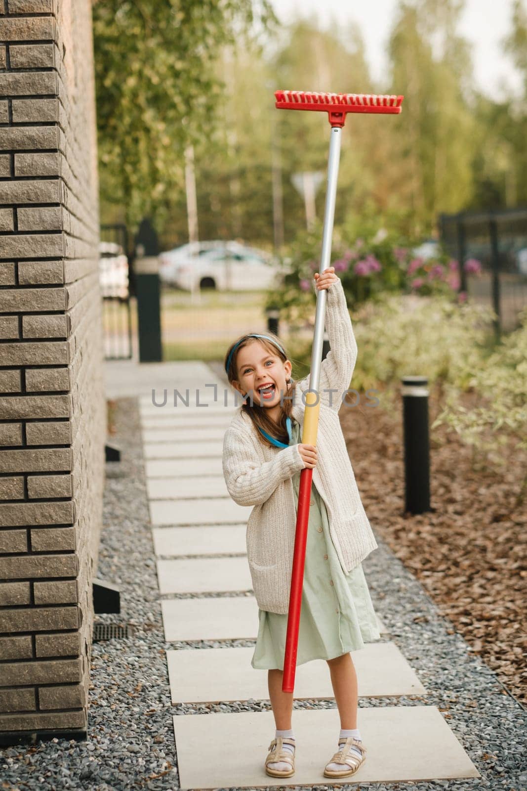 A little girl with a brush cleans a path on the street in the courtyard by Lobachad