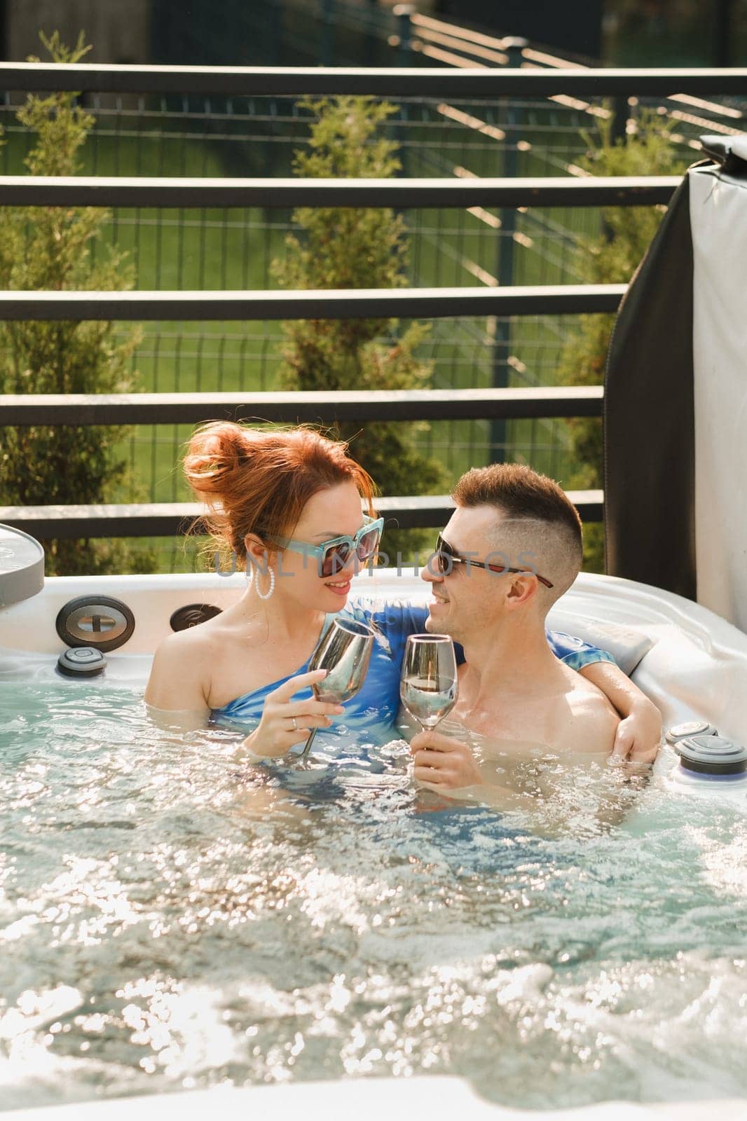 In summer, a man and a woman with glasses of wine relax in the outdoor hot tub.