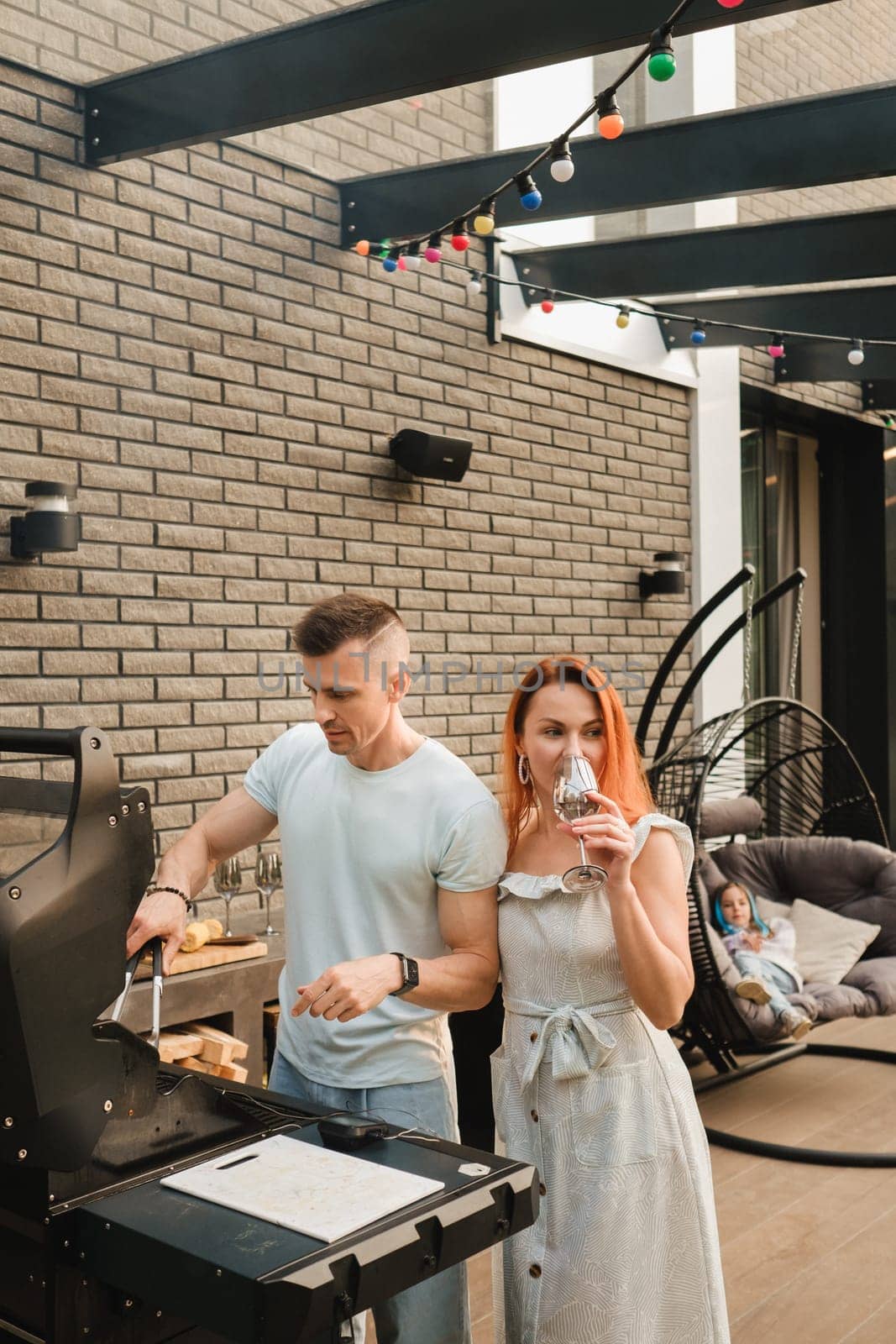 A married couple cooks grilled meat together on their terrace.