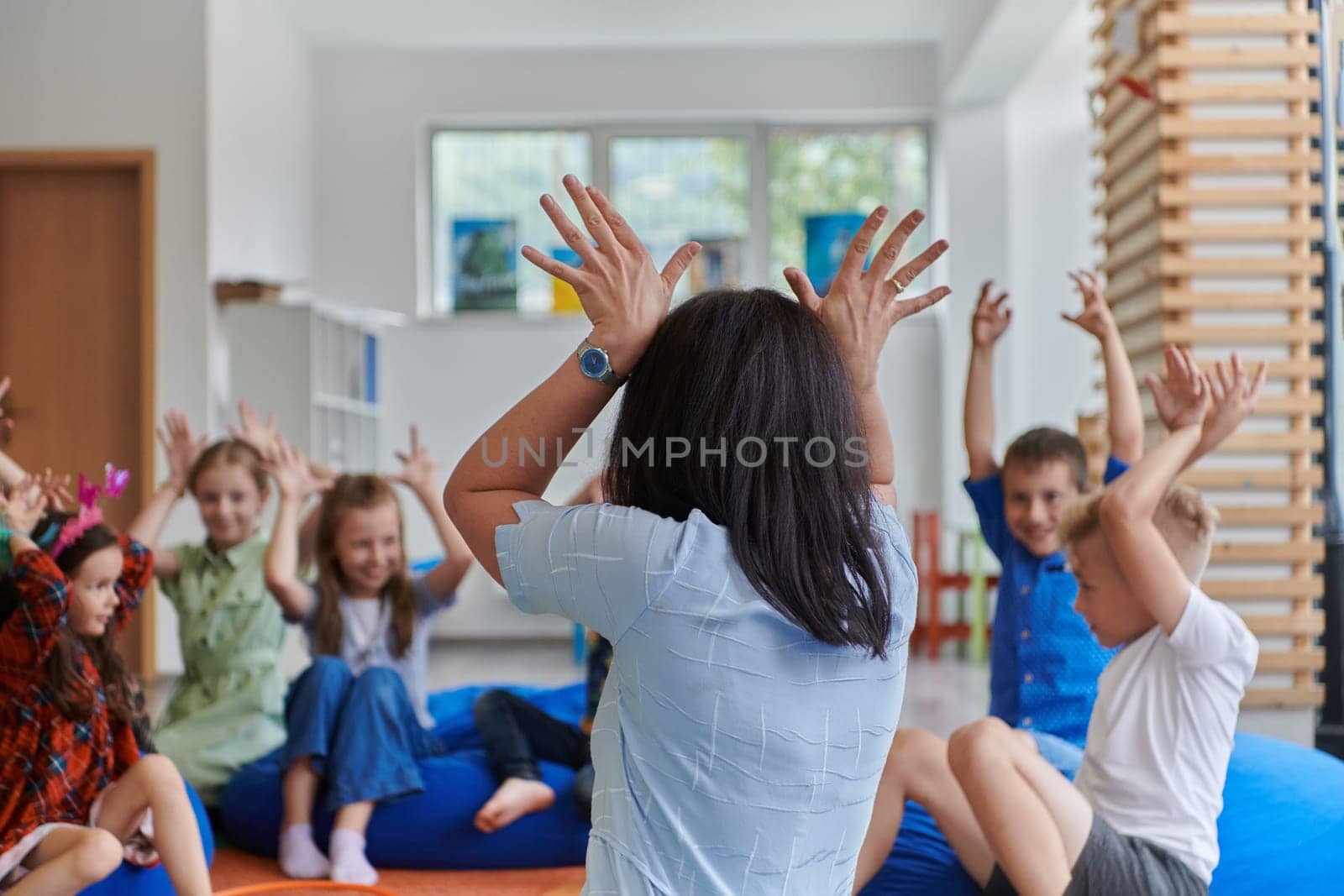 A happy female teacher sitting and playing hand games with a group of little schoolchildren by dotshock