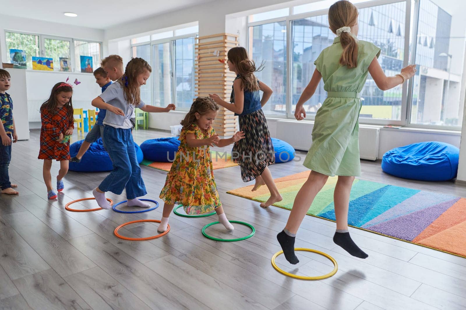 Small nursery school children with female teacher on floor indoors in classroom, doing exercise. Jumping over hula hoop circles track on the floor