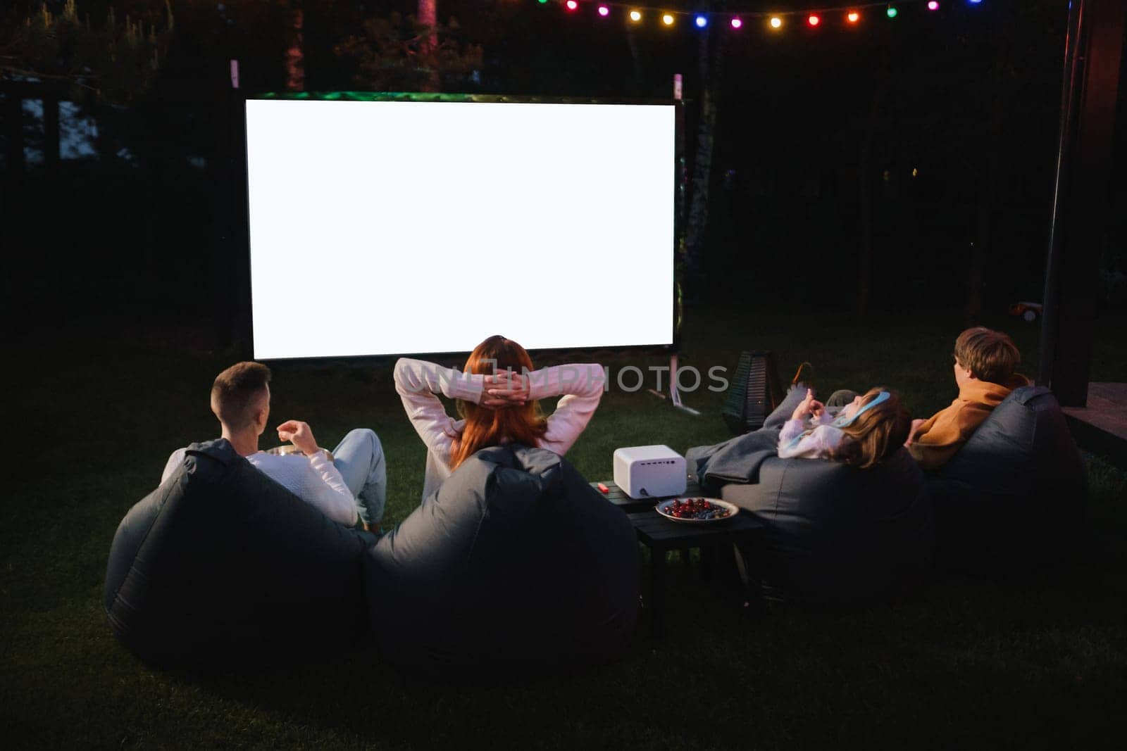 family mother, father and children watch a projector, movies with popcorn in the evening in the courtyard