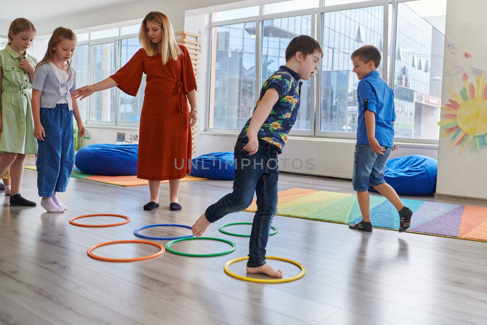 Small nursery school children with female teacher on floor indoors in classroom, doing exercise. Jumping over hula hoop circles track on the floor. by dotshock