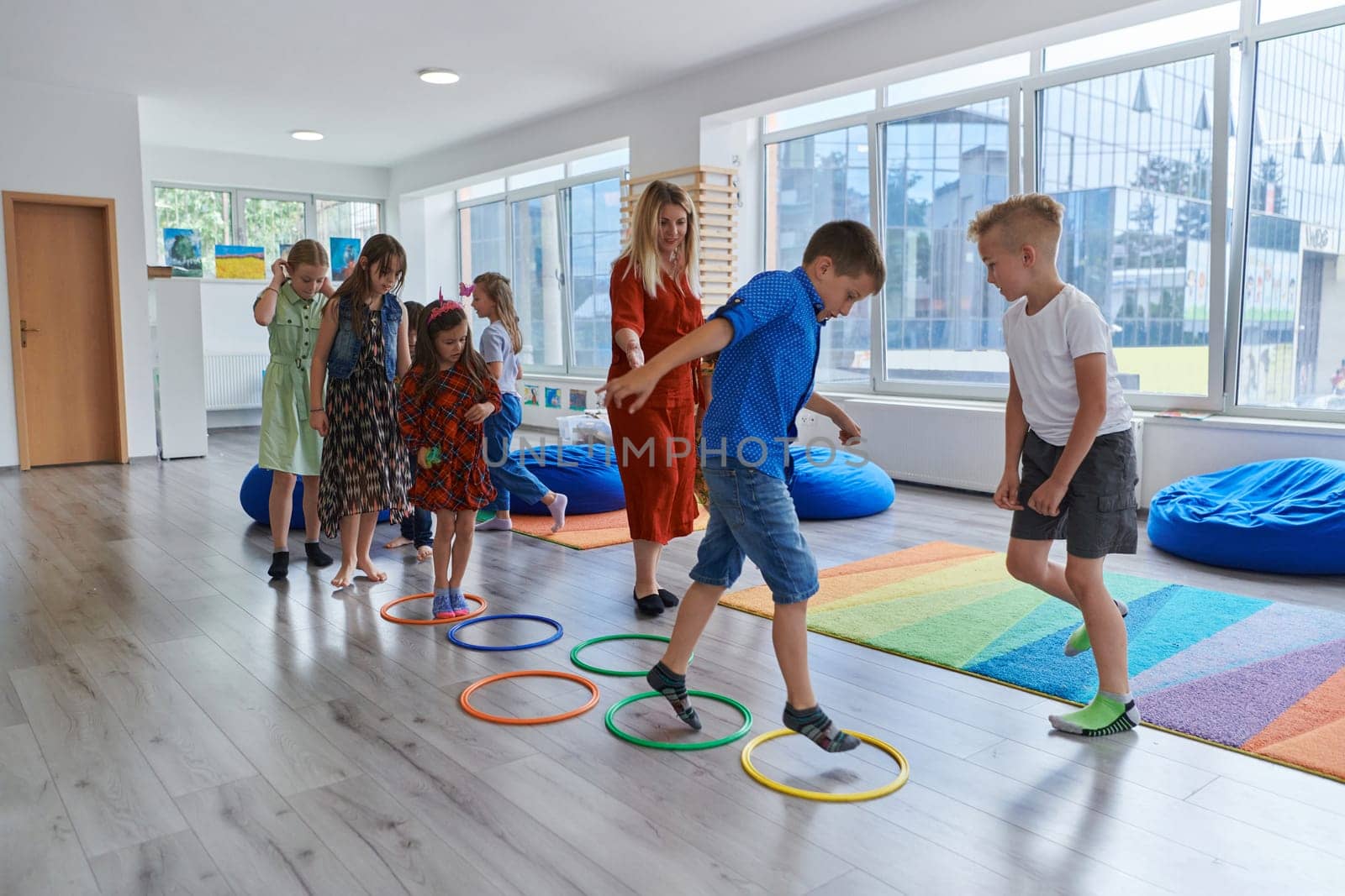 Small nursery school children with female teacher on floor indoors in classroom, doing exercise. Jumping over hula hoop circles track on the floor. by dotshock