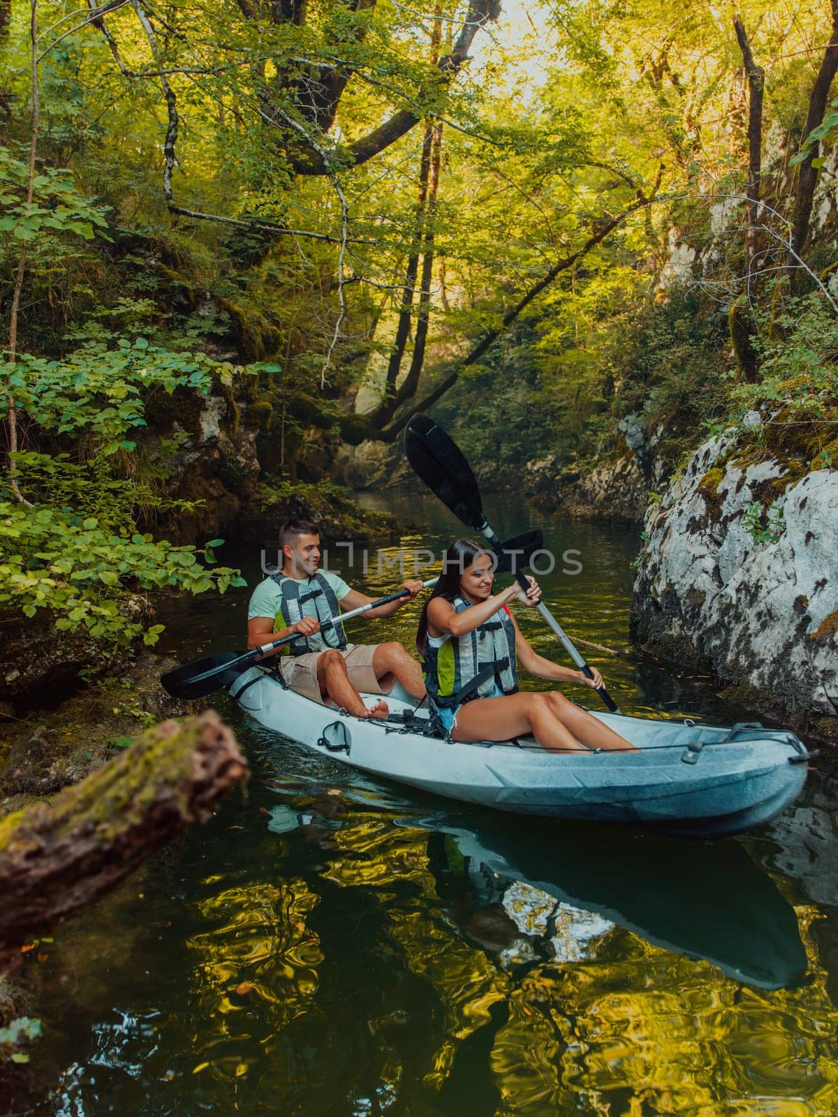 A young couple enjoying an idyllic kayak ride in the middle of a beautiful river surrounded by forest greenery by dotshock