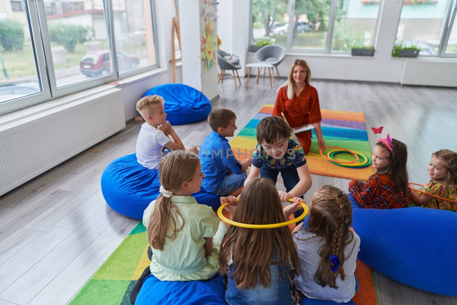 A happy female teacher sitting and playing hand games with a group of little schoolchildren by dotshock