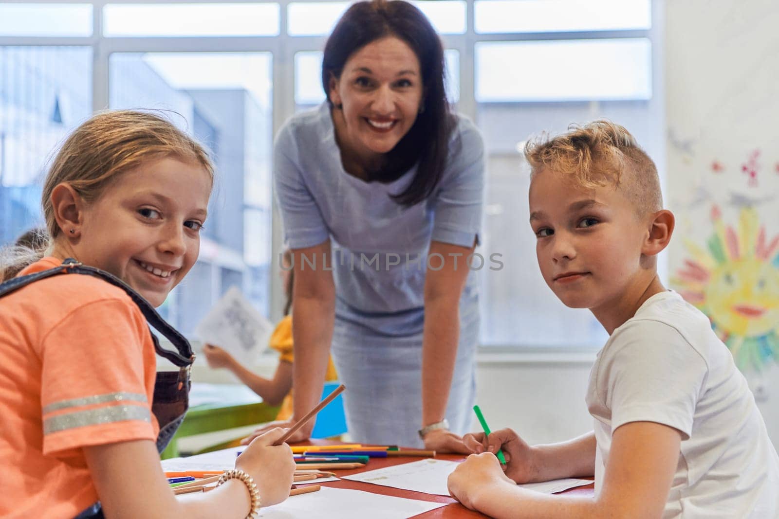 Creative kids during an art class in a daycare center or elementary school classroom drawing with female teacher