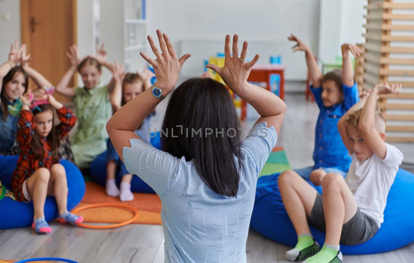 A happy female teacher sitting and playing hand games with a group of little schoolchildren by dotshock