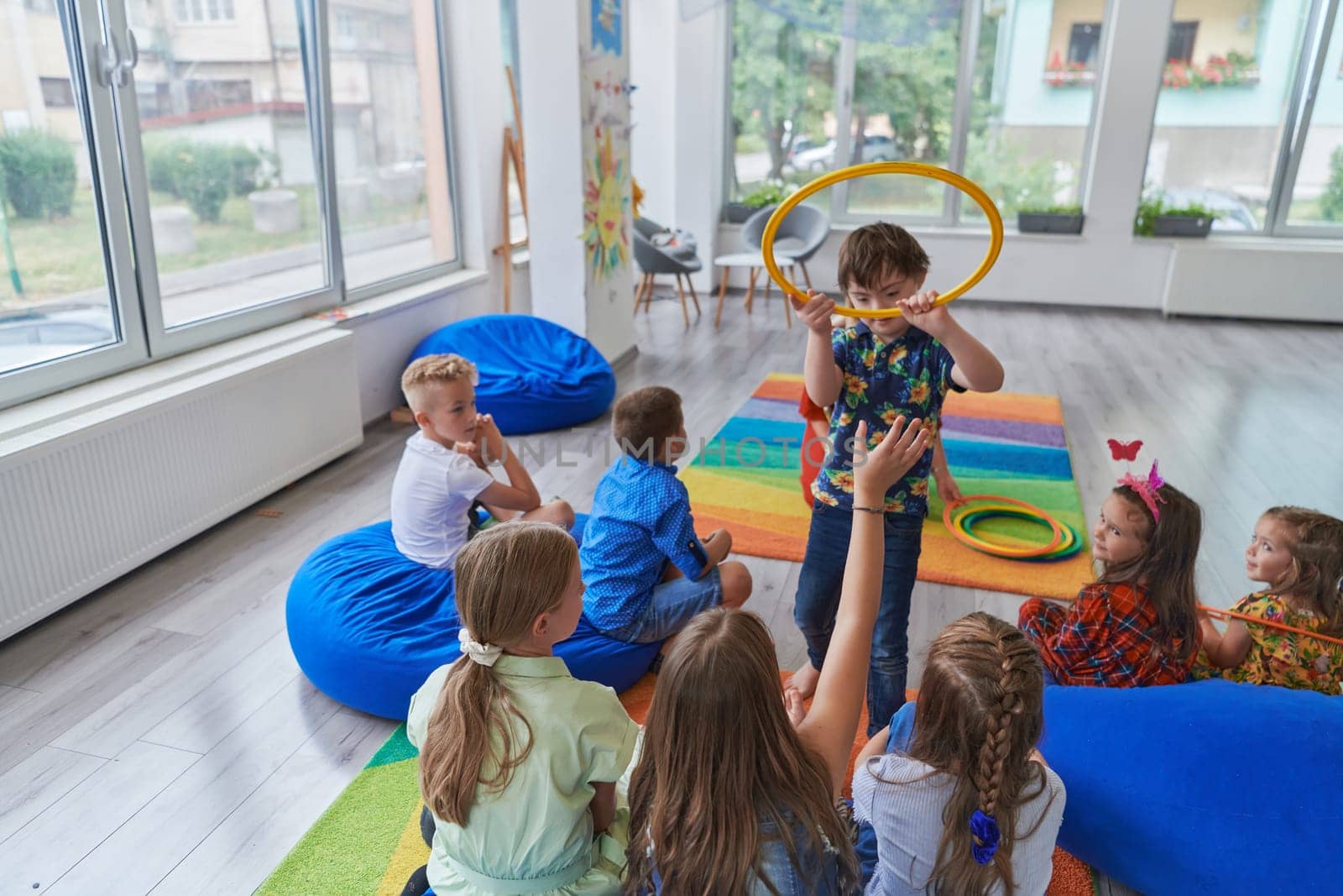 A happy female teacher sitting and playing hand games with a group of little schoolchildren by dotshock