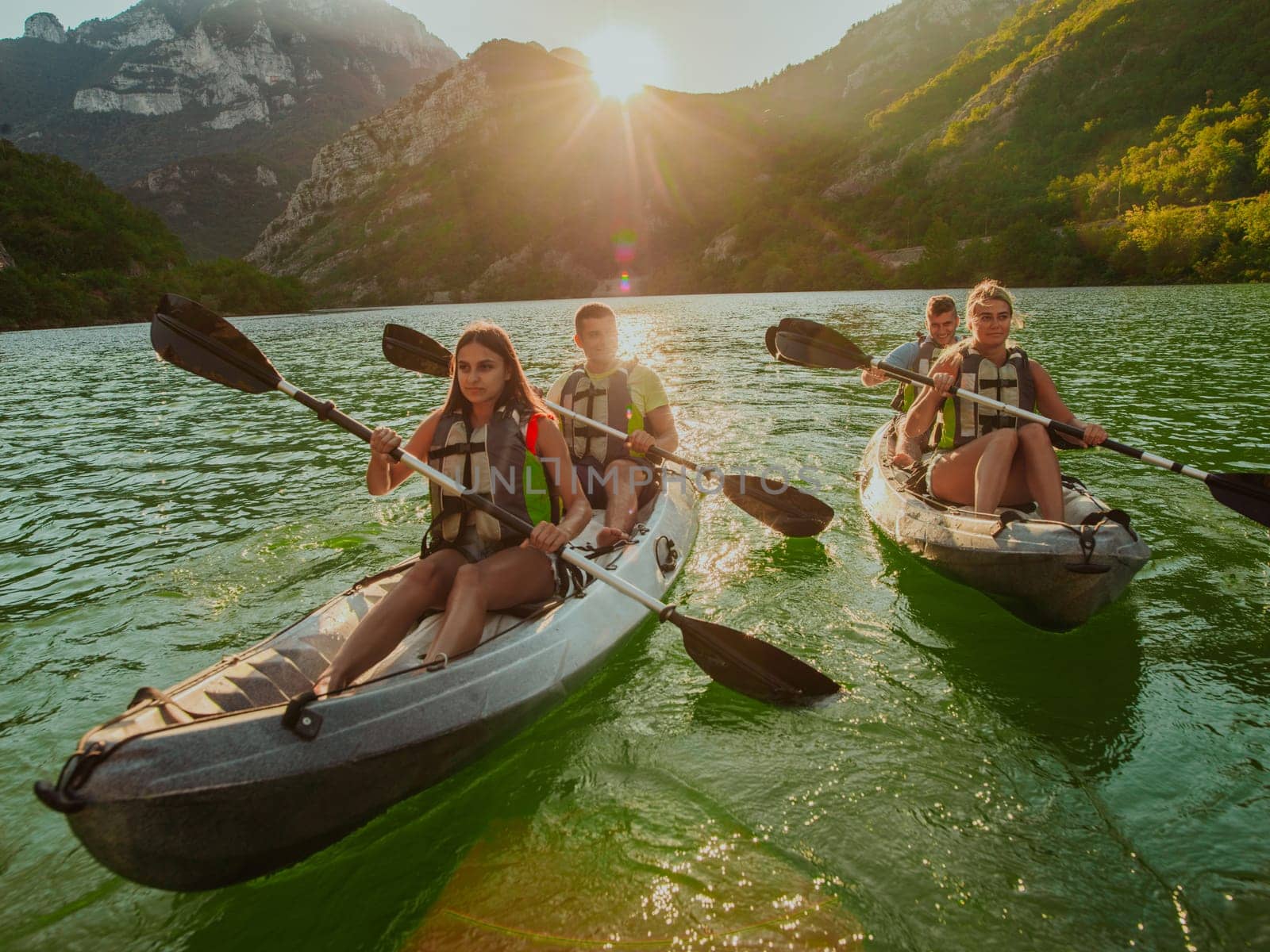 A group of friends enjoying fun and kayaking exploring the calm river, surrounding forest and large natural river canyons during an idyllic sunset