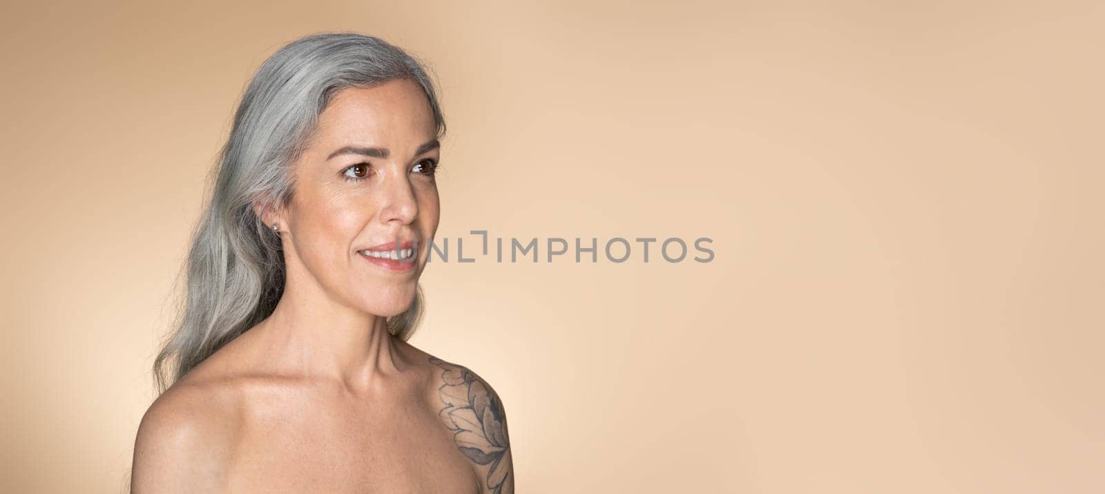 Graceful aging concept. Beautiful senior woman with glowing skin posing over beige studio background, panorama with copy space. Sensual mature woman enjoying her beauty