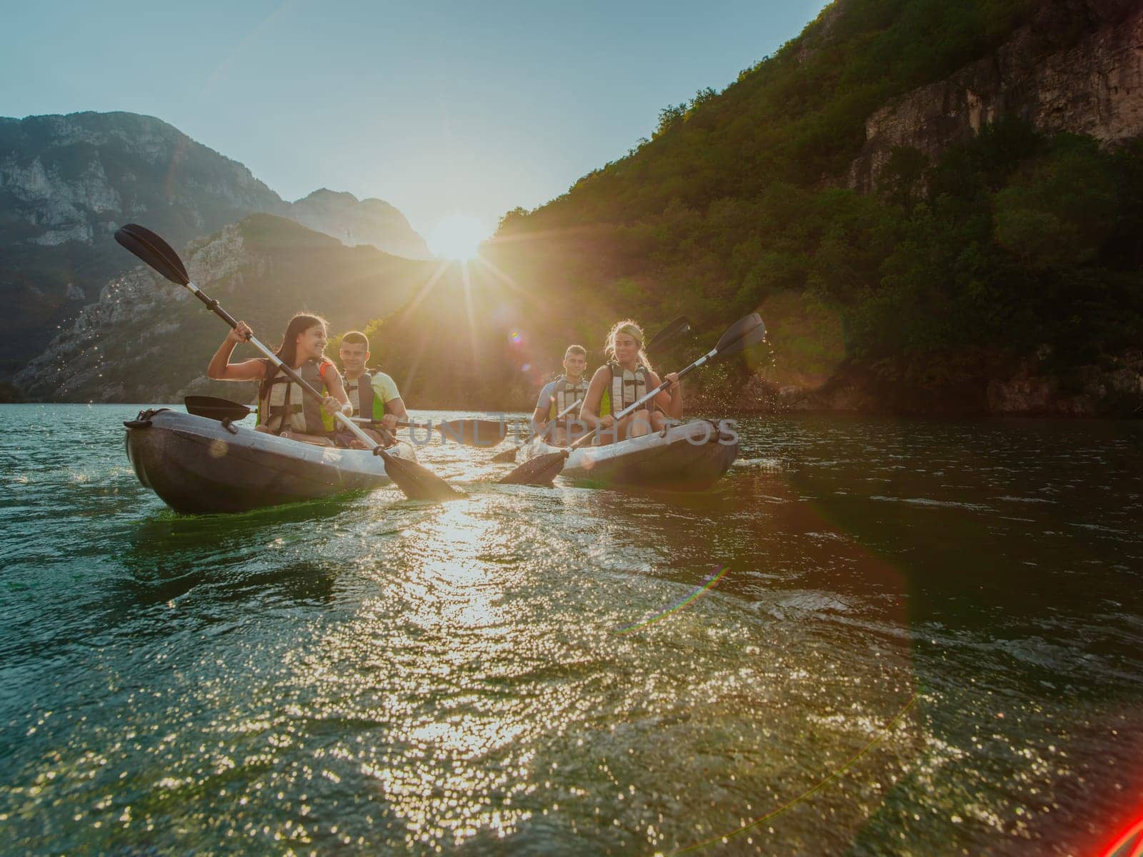 A group of friends enjoying fun and kayaking exploring the calm river, surrounding forest and large natural river canyons during an idyllic sunset. by dotshock