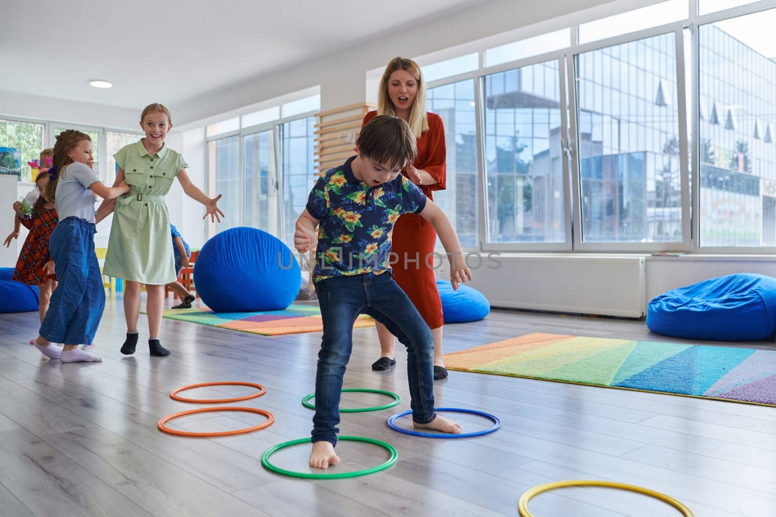 Small nursery school children with female teacher on floor indoors in classroom, doing exercise. Jumping over hula hoop circles track on the floor