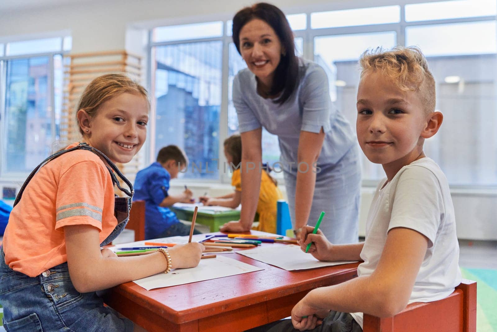 Creative kids during an art class in a daycare center or elementary school classroom drawing with female teacher