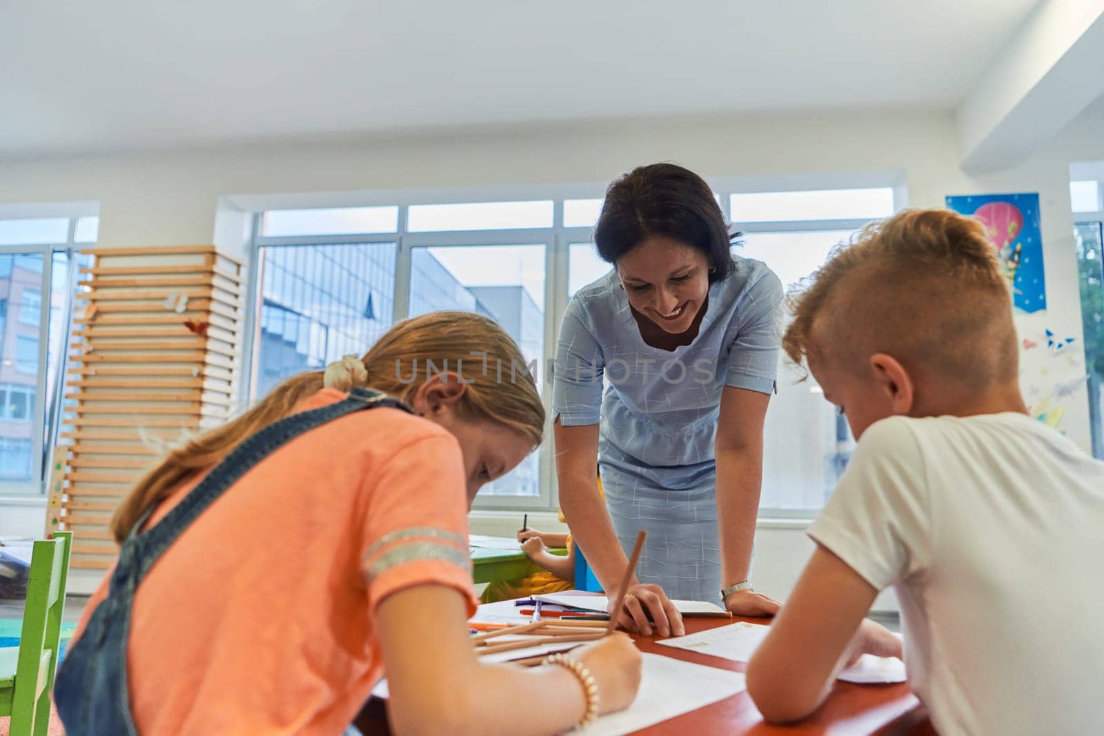 Creative kids during an art class in a daycare center or elementary school classroom drawing with female teacher