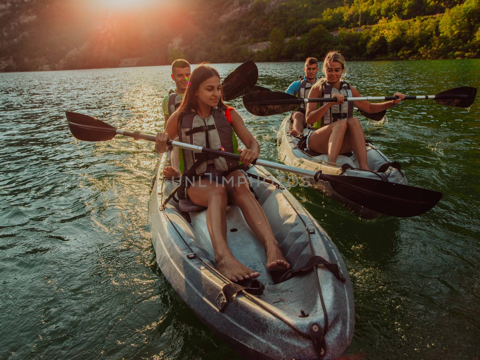 A group of friends enjoying fun and kayaking exploring the calm river, surrounding forest and large natural river canyons during an idyllic sunset