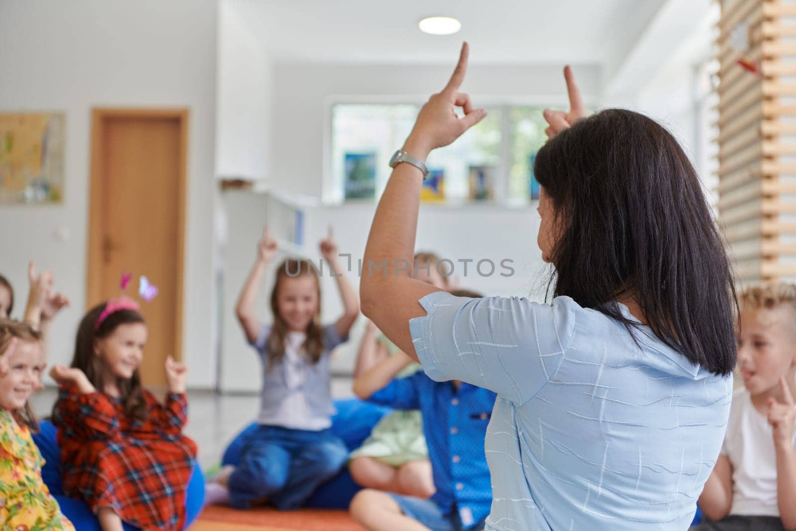 A happy female teacher sitting and playing hand games with a group of little schoolchildren.