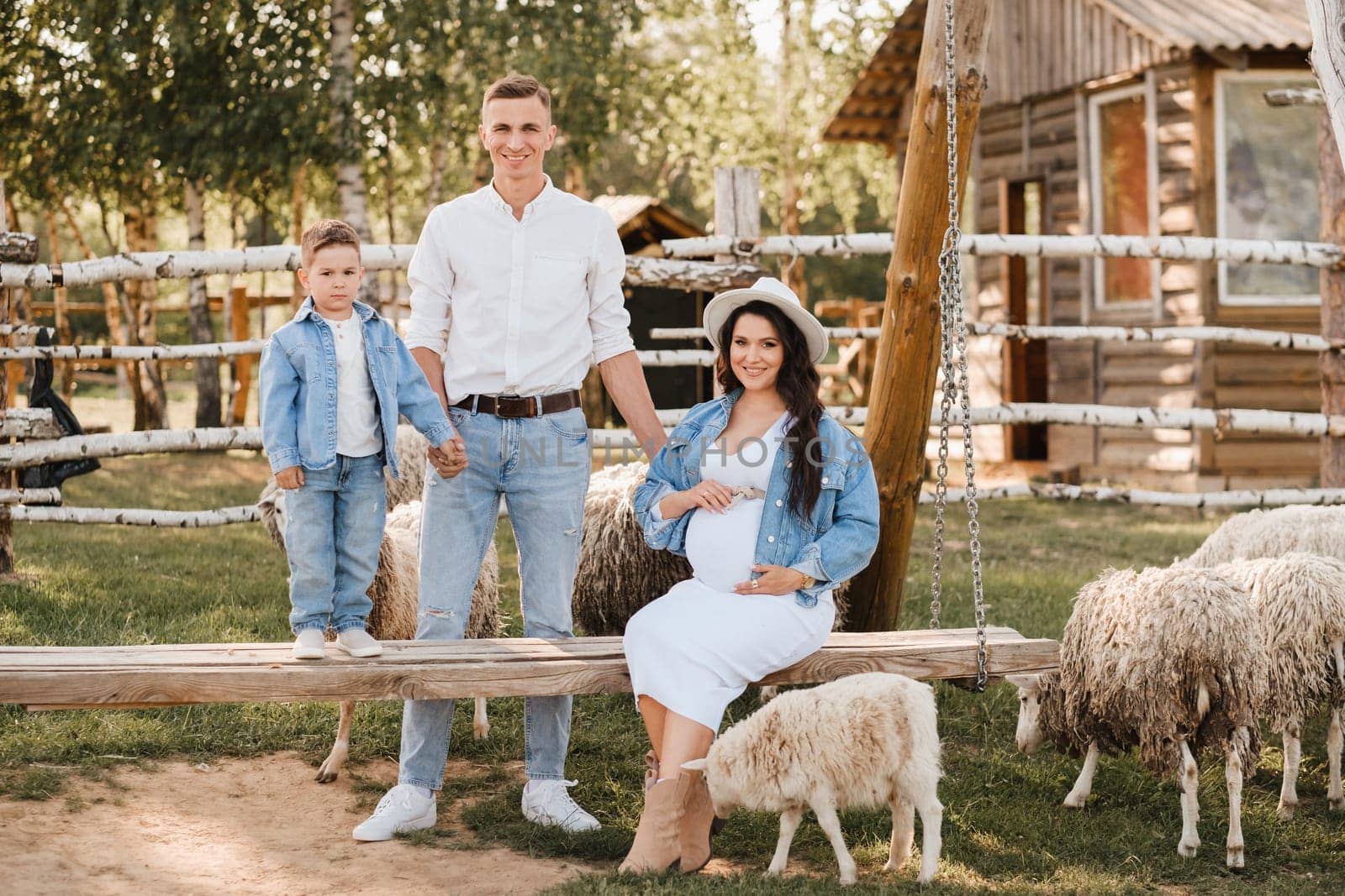 Stylish family in summer on a village farm with sheep.