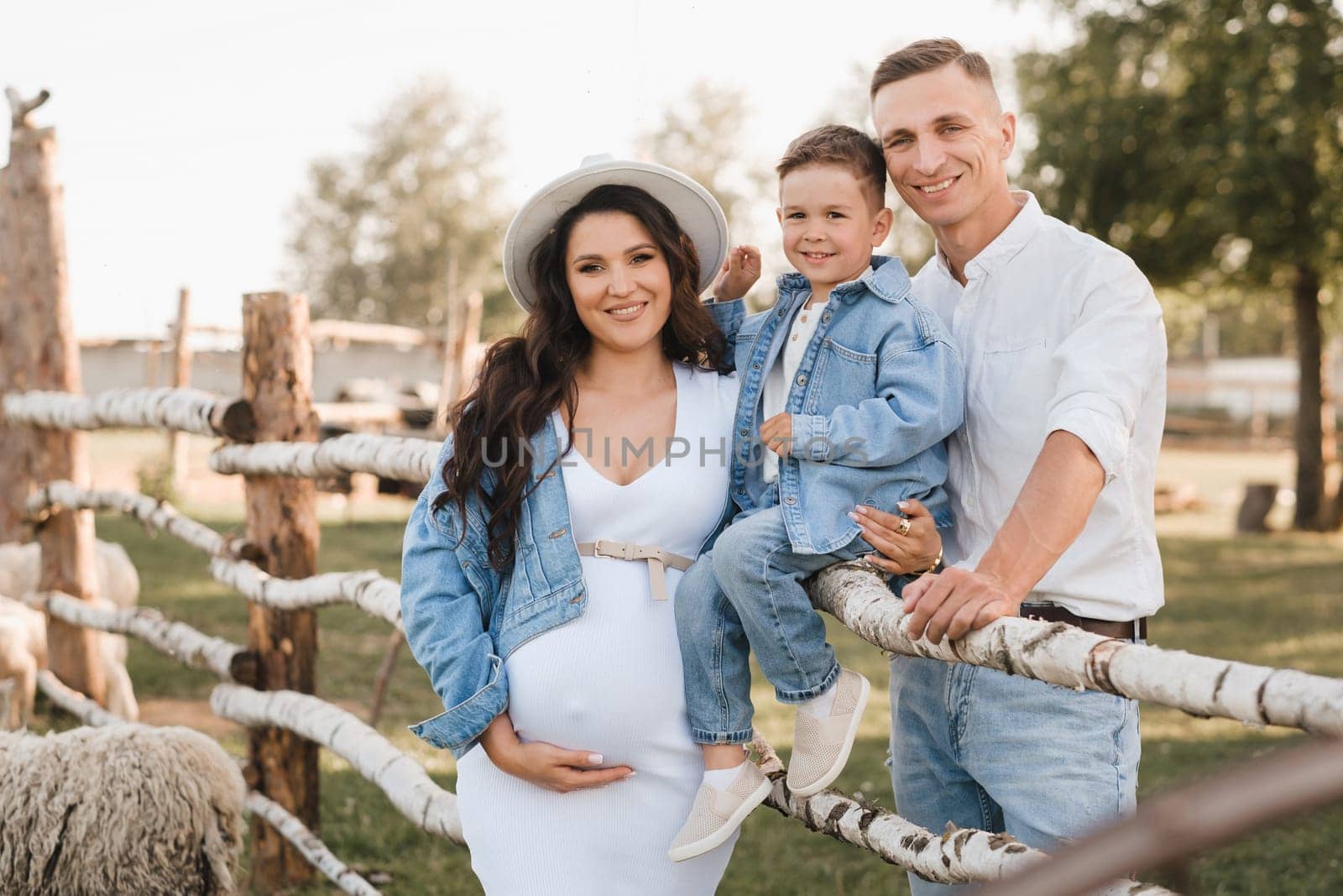 Stylish family in summer on a village farm with sheep.