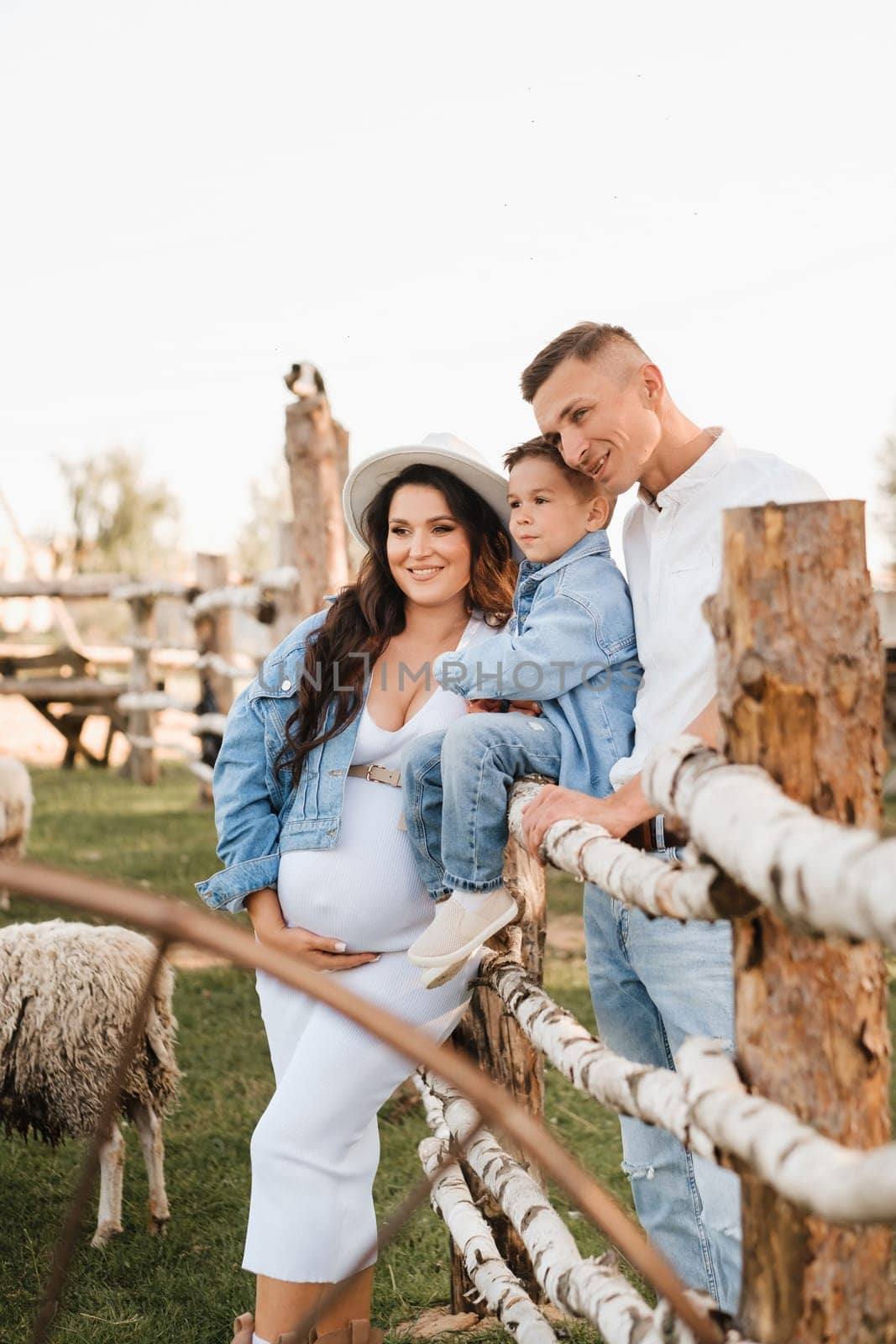 Stylish family in summer on a village farm with sheep.