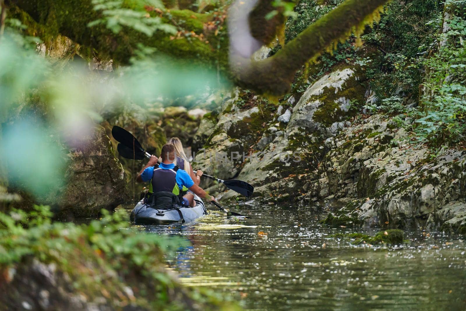 A young couple enjoying an idyllic kayak ride in the middle of a beautiful river surrounded by forest greenery by dotshock