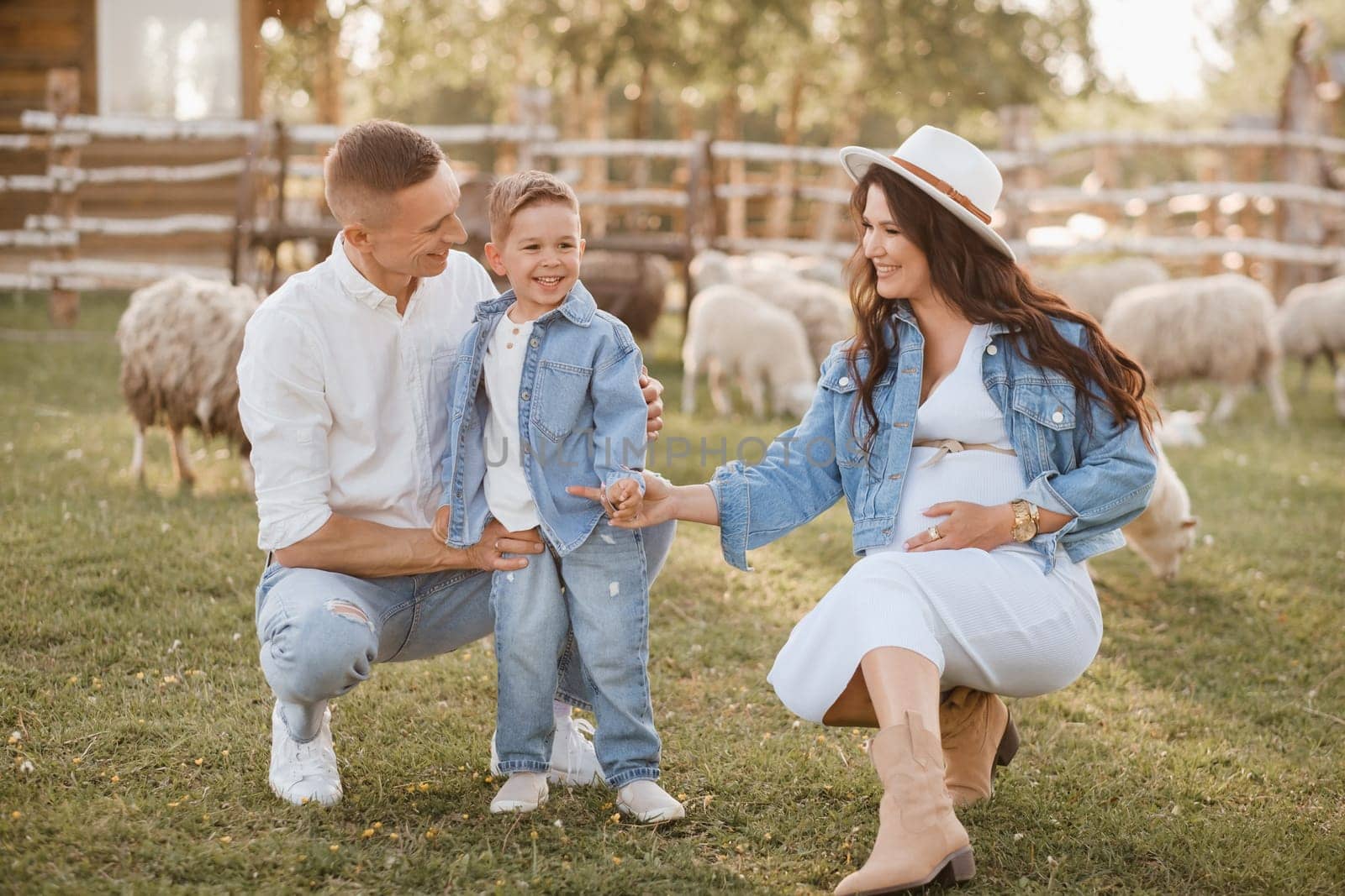 Stylish family in summer on a village farm with sheep.