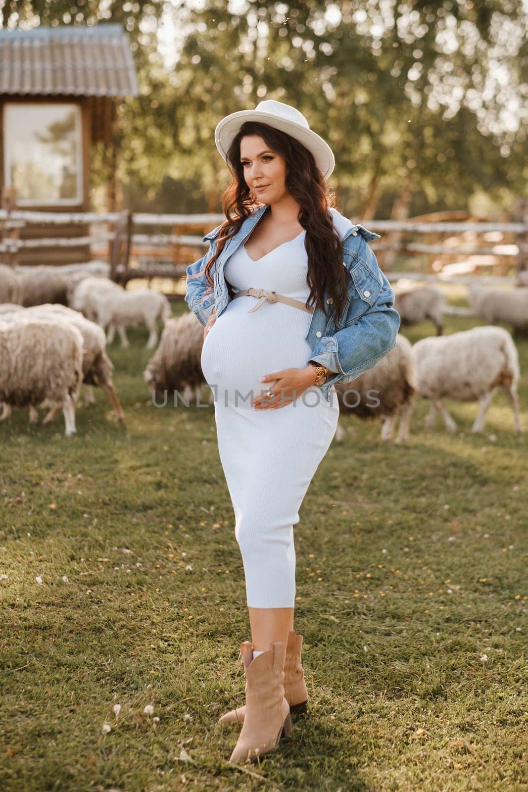 Stylish pregnant woman in a white hat in the countryside.