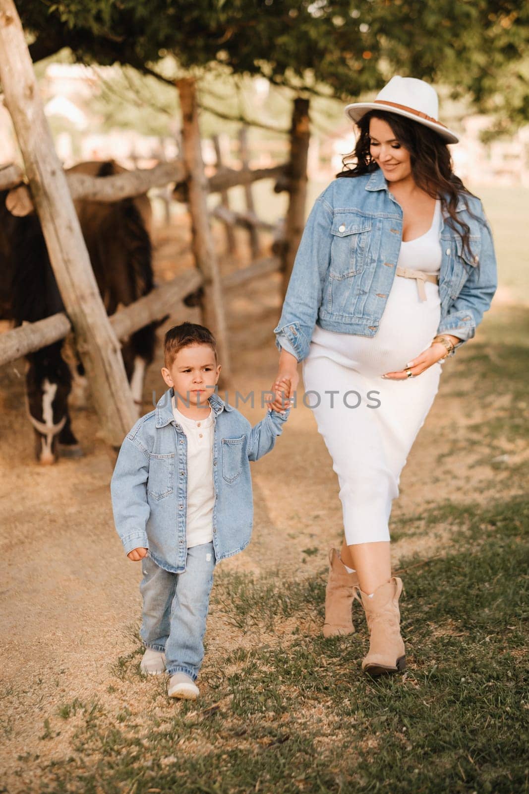 A pregnant woman with her son walks in the countryside in the summer by Lobachad
