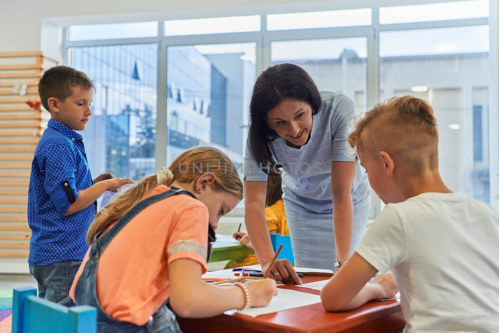 Creative kids during an art class in a daycare center or elementary school classroom drawing with female teacher